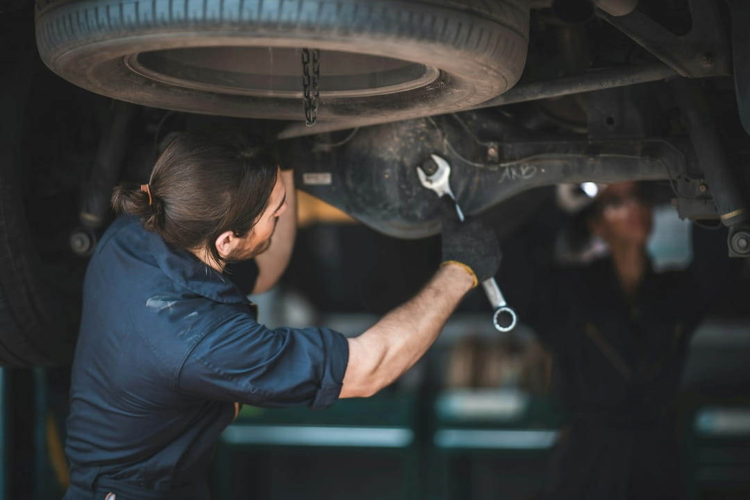 mechanic inspecting the underside of a car with a wrench